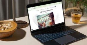A laptop displaying a homeopath's website, surrounded by a wooden bowl, a glass of herbal tea, and natural elements like greenery in the background.